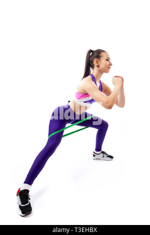 Donna sportiva non esercita sulle gambe, rende balzi in avanti con lo sport fitness bande di gomma su sfondo bianco. Foto di donna muscolare in sportswear su whi Foto Stock