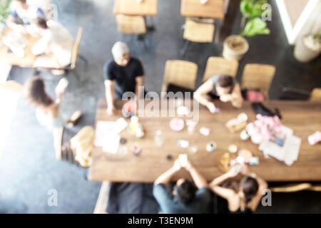 Sfocare lo sfondo delle persone nella caffetteria. Grande tavolo lungo in stile loft. Vista dall'alto. Lavoro di squadra concetto. Foto Stock