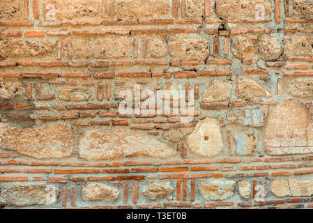 Texture orizzontale di antico muro di pietra dalla diversa forma delle pietre. Superficie dal grigio e arancione pietre. Vecchio muro in Macedonia Foto Stock