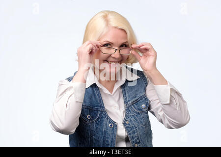 Senior donna occhiali di regolazione e sorridente a voi Foto Stock