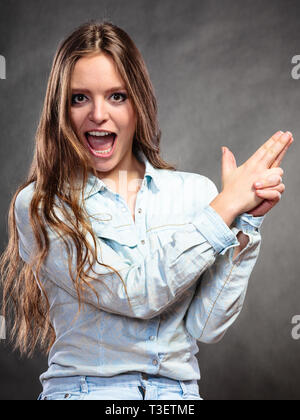 Donna felice divertendosi e ingannare circa fingendo la sua mano dito è una pistola. Ragazza gioiosa hanno bel tempo. Foto Stock