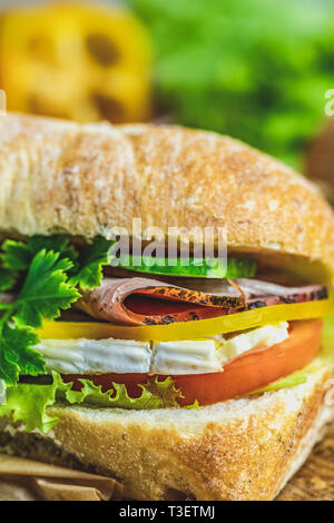 La ciabatta in sandwich con prosciutto e pomodoro, formaggio, pepe, cipolla e insalata sul tagliere di legno con ingredienti. Foto Stock