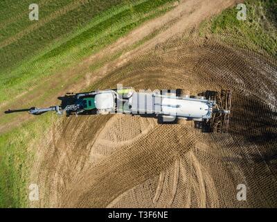 Vista aerea di un trattore con un moderno rimorchio di fertilizzante e un secondo trattore con un fertilizzante liquido il rimorchio su un campo agricolo Foto Stock