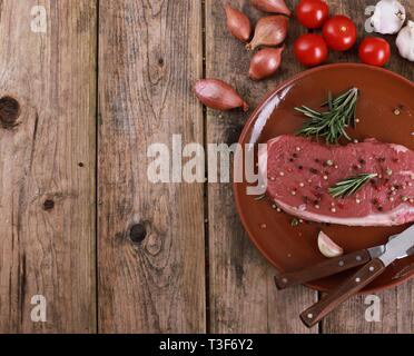 Materie rumpsteak bistecca con rosmarino, pepe, pomodori e spezie su una tavola in legno rustico Foto Stock