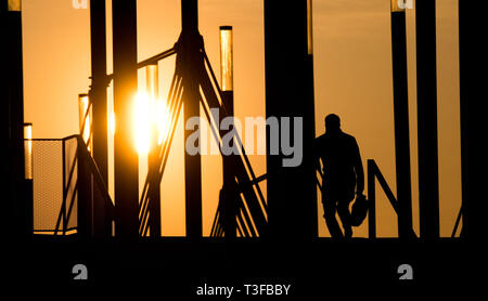 Hannover, Germania. 09Apr, 2019. Un uomo cammina su un ponte a Expo Plaza con una valigetta di sunrise. Credito: Julian Stratenschulte/dpa/Alamy Live News Foto Stock