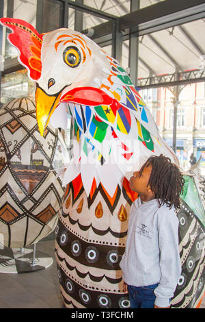 Gigantesco pollo di carta pasquale oversize in esposizione nel centro della città. TADIWA CHAPARADZA (MR) 10 anni è incuriosito dalla grande scultura di scarafaggio Papier-Mache. Le figure degli animali natalizi di Pasqua in mostra, alte due metri, le attrazioni sono collocate fuori dal mercato di Preston. Keith Ogden, un artista locale, è l'uomo dietro l'attrazione dipinta a mano. Le uova sono a tema intorno al patrimonio industriale della città e paesaggi Lancashire. I mercati di Preston espongono le uova di Pasqua giganti per la competizione di selfie durante le vacanze di Pasqua. Foto Stock