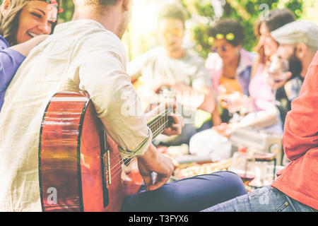 Gruppo di amici avente un picnic in un parco outdoor - Happy giovani si accoppia godendo di pic-nic a suonare la chitarra e cantare e bere vino mangiando cibo Foto Stock