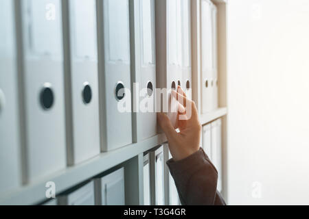 Imprenditrice navigando attraverso il ring binder file archivio di documentazione o il ripiano in ufficio business, stretta di mano Foto Stock