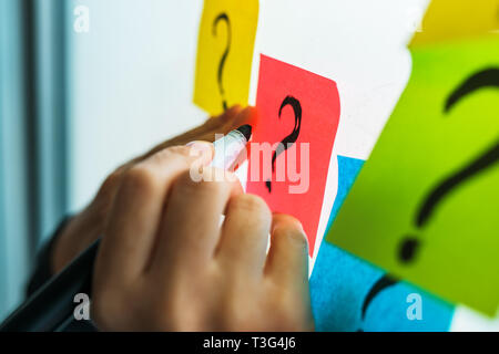 Imprenditrice iscritto interrogativi sulla colorata nota adesiva carta su office whiteboard, il fuoco selettivo Foto Stock