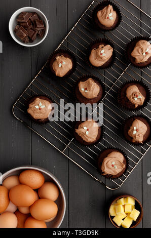 Torte di Fairy su un vassoio di raffreddamento con ingredienti, su un invecchiato in legno grigio Sfondo, ripresa dall'alto Foto Stock