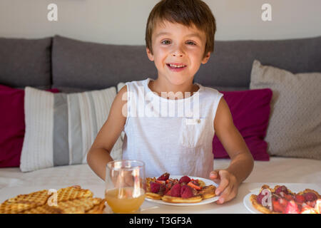 Dolce ragazzo di compleanno, mangiare i waffle belgi con fragole e lamponi e il cioccolato a casa
