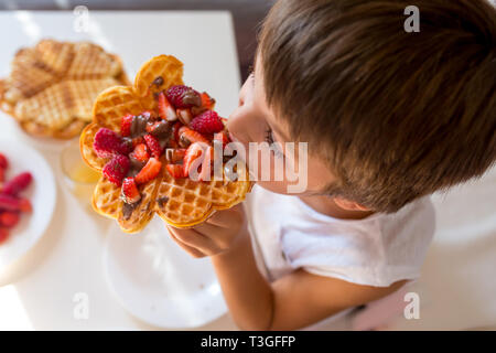 Dolce ragazzo di compleanno, mangiare i waffle belgi con fragole e lamponi e il cioccolato a casa Foto Stock