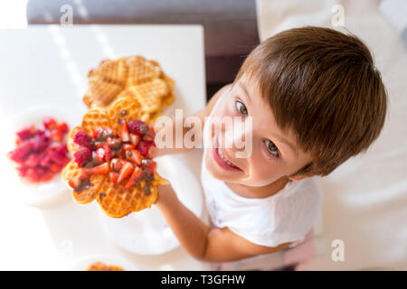 Dolce ragazzo di compleanno, mangiare i waffle belgi con fragole e lamponi e il cioccolato a casa