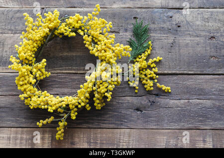 Ghirlanda di fiori di acacia e succursale in legno rustico sfondo. Acacia dealbata. Spazio per scrivere. Foto Stock