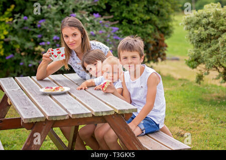 Madre e tre bambini avente il tè del pomeriggio nel cortile della loro casa bella vista del paesaggio di North Devon dietro di loro Foto Stock