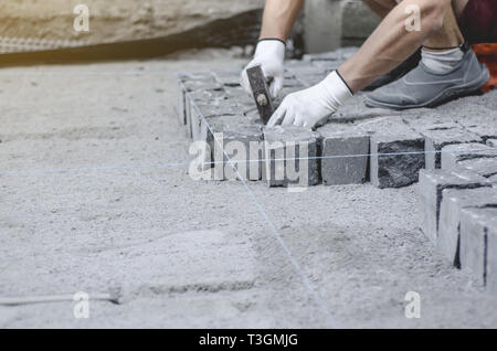 Lavoratore stabilisce il granito grigio pavimentazione piastrelle sul sito contrassegnato. Disposizione di ambiente urbano. La riparazione delle strade di città Foto Stock