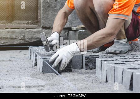 Lavoratore stabilisce il granito grigio pavimentazione piastrelle sul sito contrassegnato. Disposizione di ambiente urbano. La riparazione delle strade di città Foto Stock