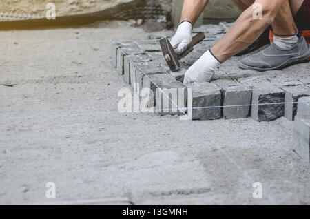 Lavoratore stabilisce il granito grigio pavimentazione piastrelle sul sito contrassegnato. Disposizione di ambiente urbano. La riparazione delle strade di città Foto Stock