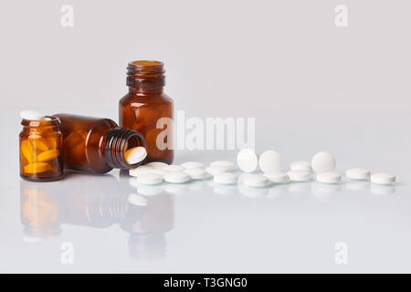 White compresse e pillole in vetro scuro bottiglia su sfondo bianco. Health care concetto. Supplementi diffusa dal vetro bottiglia marrone Foto Stock