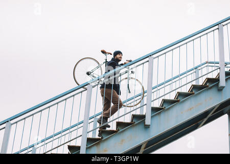 Sorridente ragazzo barbuto che porta bicicletta sulle spalle Foto Stock