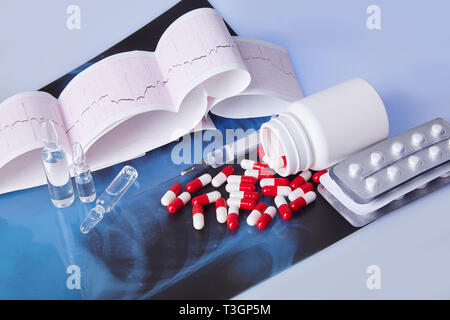 Sparse in capsule, compresse, fiale e la siringa sul tavolo con cardiogram grafico ecg (mi) e di Roentgen. Il concetto di assistenza sanitaria. Cardiogram stampa. Foto Stock