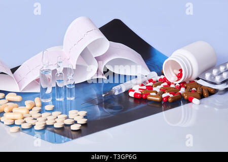 Sparse in capsule, compresse, fiale e la siringa sul tavolo con cardiogram grafico ecg (mi) e di Roentgen. Il concetto di assistenza sanitaria. Cardiogram stampa. Foto Stock