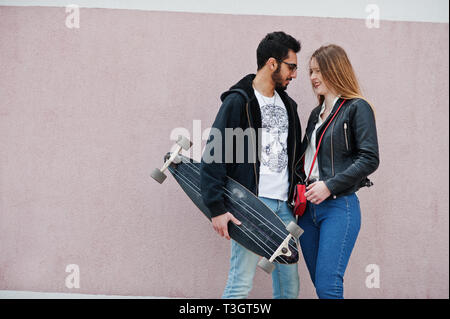 Cool multirazziale matura in posa contro la parete rosa con longboard. Foto Stock