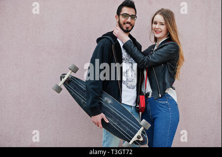 Cool multirazziale matura in posa contro la parete rosa con longboard. Foto Stock