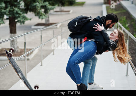 Cool multirazziale matura in posa con longboard e abbracci insieme. Foto Stock