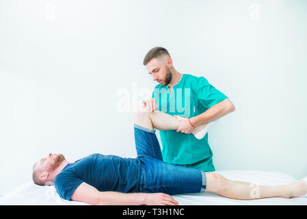 Giovane maschio massaggio di ricezione dal terapista. Un chiropratico stretching la sua gambe del paziente in ufficio medico. Neurologiche esame fisico. Osteop Foto Stock