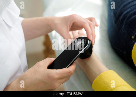 Il dermatologo femmina usando un professionista dermatoscope mentre si esegue un esame della pelle, controllo benigne moli sulla mano. Il dermatologo esaminando birthmarks Foto Stock