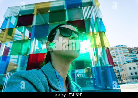 Spagna, Malaga - 04.04.2019: Donna ritratto astratto in rayban occhiali da sole accanto al cubo colorato Centro Pompidou a Malaga, Spagna nella luce del sole Foto Stock