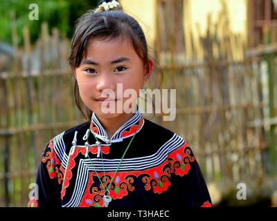 Piuttosto pre-teen Miao ragazza (Cinese minoranza etnica) indossa un rosso e nero tradizionale abito etnici e sorrisi per la fotocamera. Foto Stock