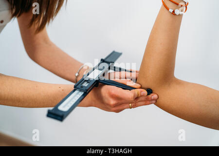 Medico tenendo il corpo del paziente le misurazioni del grasso sul braccio con pinza di grasso Foto Stock