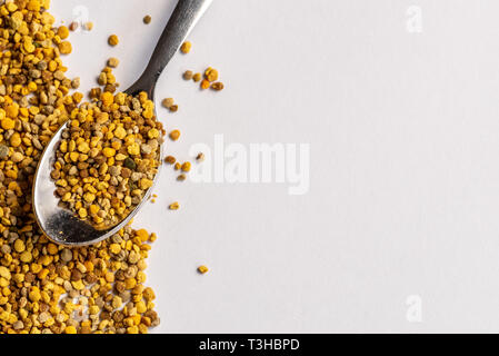 Granuli di polline di api su un foglio di carta bianca con un cucchiaino da caffè di granuli, copyspace Foto Stock