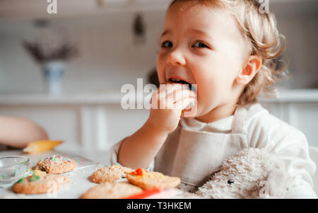 Un piccolo bambino ragazza seduta al tavolo, decorare torte a casa. Foto Stock