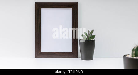 Vuoto dark photo frame e due succulente in vasi scuri su uno sfondo bianco. Lo stile scandinavo MockUp Foto Stock