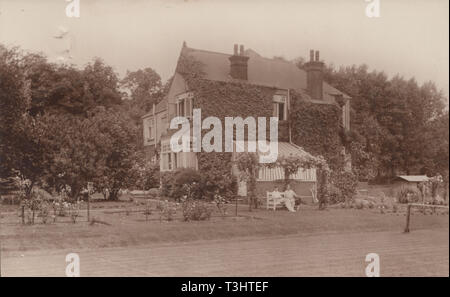 L'annata 1929 Middlesex Cartolina fotografica che mostra una grande British staccato Home. Giovane rilassante su un banco di lavoro con il loro vasto giardino Foto Stock