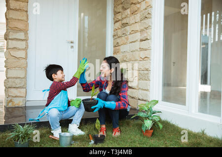 Madre e figlio highfive mentre il giardinaggio insieme a casa Foto Stock