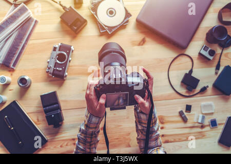 Vista superiore del fotografo femmina tenendo la fotocamera digitale al di sopra della scrivania del suo studio fotografico Foto Stock