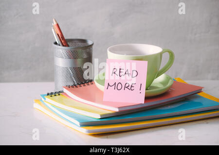 Tazza verde, notebook e un adesivo con il testo - Per saperne di più su sfondo chiaro. Nei toni del concetto di business con spazio di copia Foto Stock