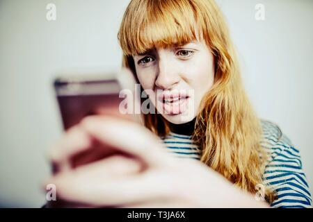 Ragazza adolescente, i capelli rossi, guarda inorridito al suo smartphone, studio shot, Germania Foto Stock