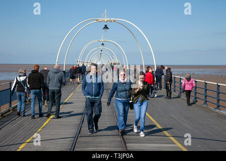 Famiglie che camminano sul molo a Southport, Regno Unito. 10th aprile 2019. Meteo Regno Unito. Soleggiato ma artico chill sulla costa con venti orientali portando basse temperature per gli escursionisti sul molo di mare. Credit: MediaWorldImages/Alamy Live News Foto Stock