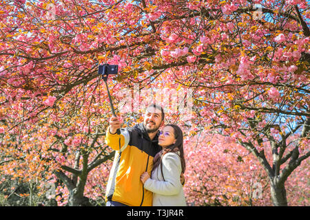 Greenwich, Londra, UK, 10 aprile 2019. Un paio di prendere selfies con graziosi fiori. Persone da ammirare e prendere scatta di rosa fiori di ciliegio che ora è in piena fioritura. I visitatori viaggiano spesso soprattutto per vedere il ben noto 'Cherry Blossom Alley' nel parco di Greenwich, Londra. Credito: Imageplotter/Alamy Live News Foto Stock