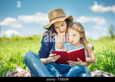 Madre e figlia di lettura sul libro verde prato estivo Foto Stock