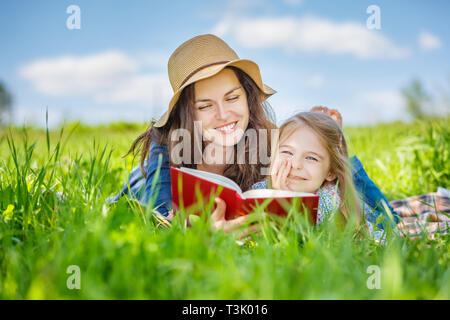 Madre e figlia di lettura sul libro verde prato estivo Foto Stock