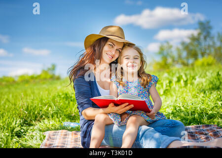 Madre e figlia di lettura sul libro verde prato estivo Foto Stock