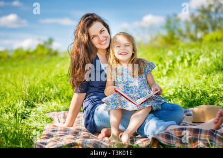 Madre e figlia di lettura sul libro verde prato estivo Foto Stock