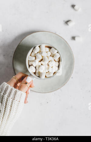 La mano della bambina detiene una tazza di cioccolata calda con marshmallow testurizzato su sfondo bianco. Stile minimalista, vista dall'alto, copia dello spazio. Foto Stock