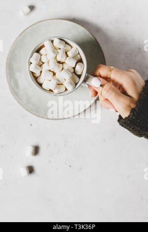 La mano della bambina detiene una tazza di cioccolata calda con marshmallow testurizzato su sfondo bianco. Stile minimalista, vista dall'alto, copia dello spazio. Foto Stock